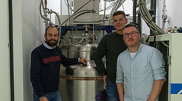 Tobias Utikal with Matthias Freudensprung, head of purchasing and Adrian Thoma, head of the building technology department in front of the new helium liquefaction system.