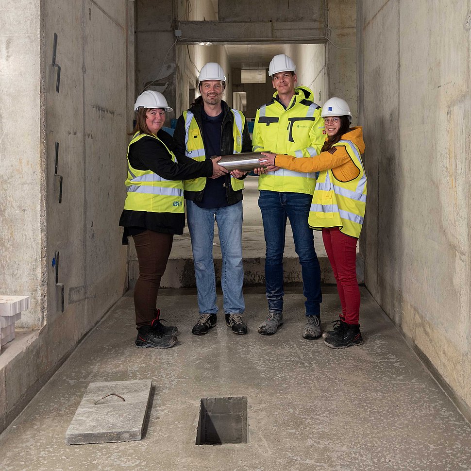 (1) Prof. Kristian Franze, Dr. Dorothe Burggraf, Adrian Thoma und Katharina Kißner versammeln sich um die MPZPM-Zeitkapsel, bevor diese in den Betonboden eingelassen wird.